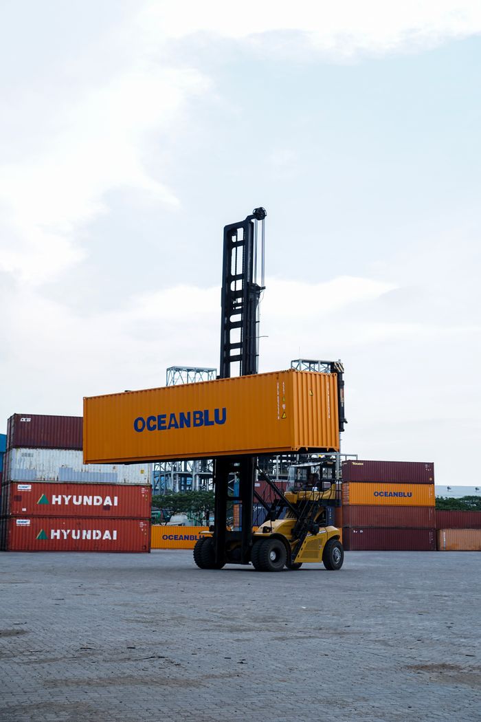 Home Forklift handling container in bustling Jakarta port with clear skies.