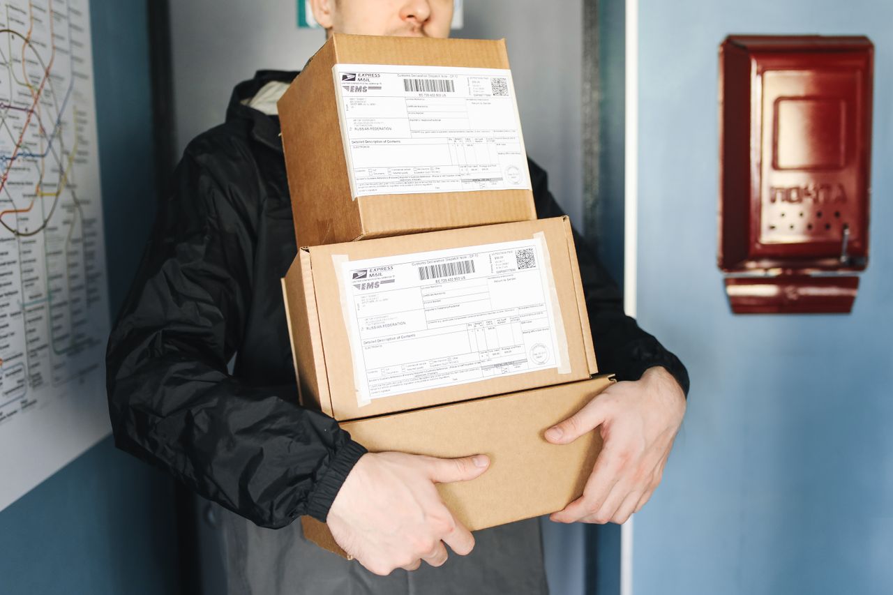 Courier carrying stacked cardboard packages for delivery service indoors.