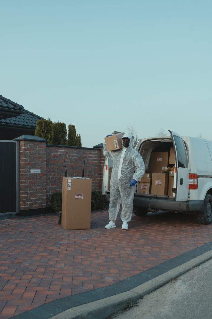 Home A delivery person in protective gear unloading packages from a van outdoors.