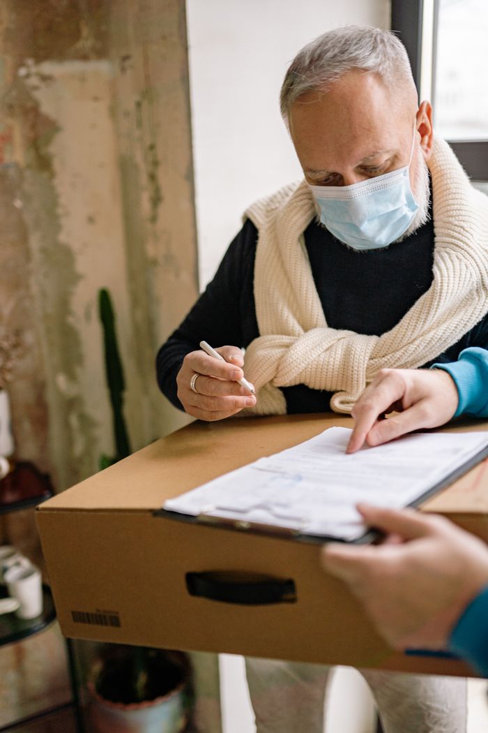 Home A person receives a package with a document and wears a medical mask indoors.